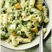 Top down partial view of broccoli pasta with garlic slices and spoon inside green bowl.