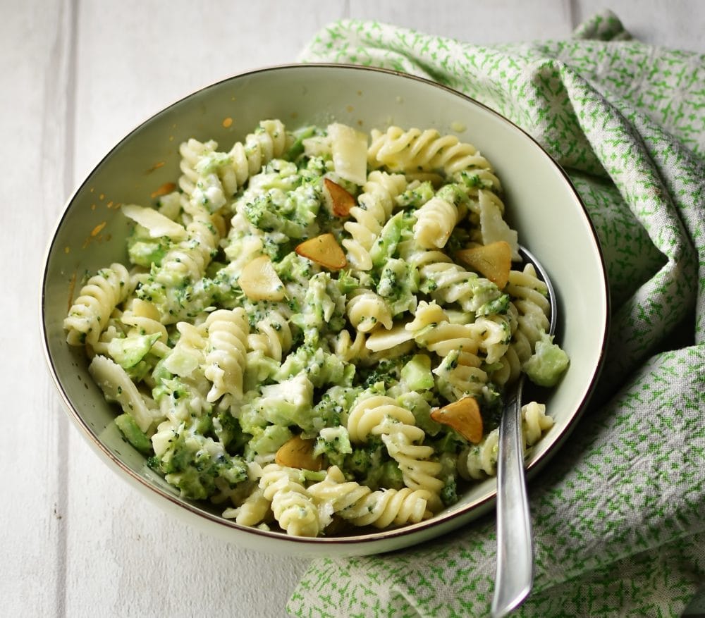 Broccoli pasta with spoon in light green coloured bowl wrapped in green cloth.