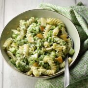 Broccoli pasta with spoon in light green coloured bowl wrapped in green cloth.