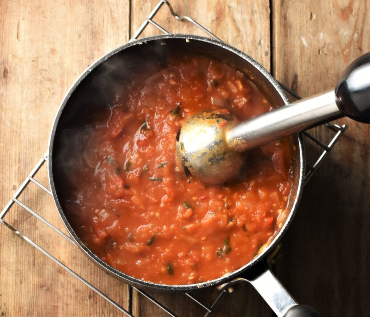 Partly pureed tomato sauce in pot with hand blender end piece.