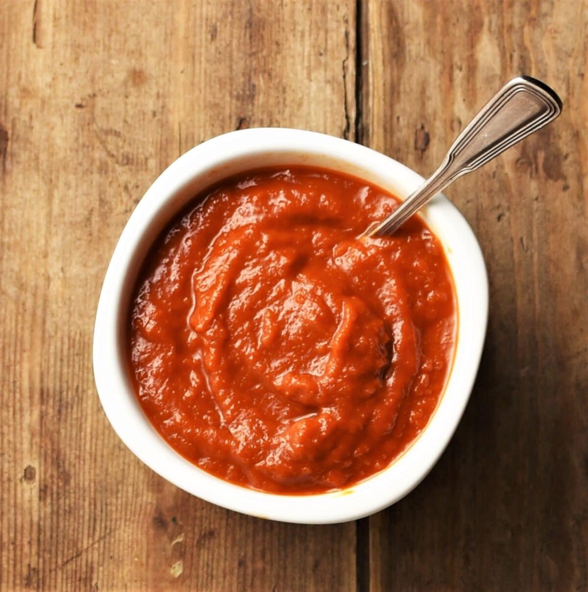 Top down view of homemade bbq sauce in white dish with spoon.