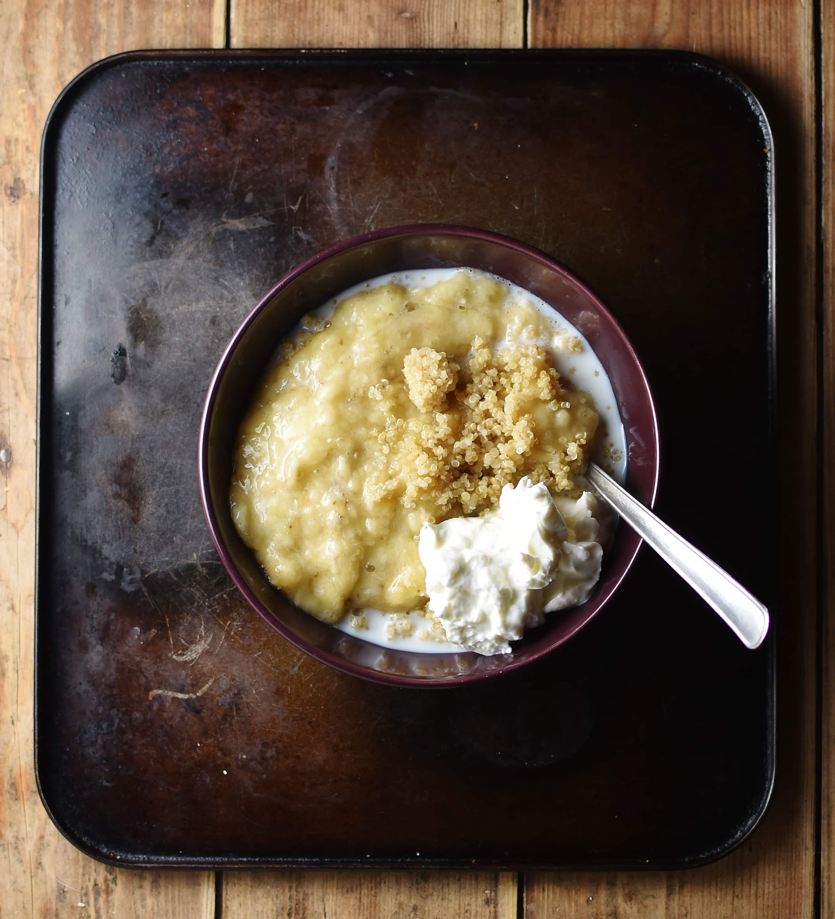 Top down view of mashed banana, yogurt and quinoa in purple bowl with spoon.