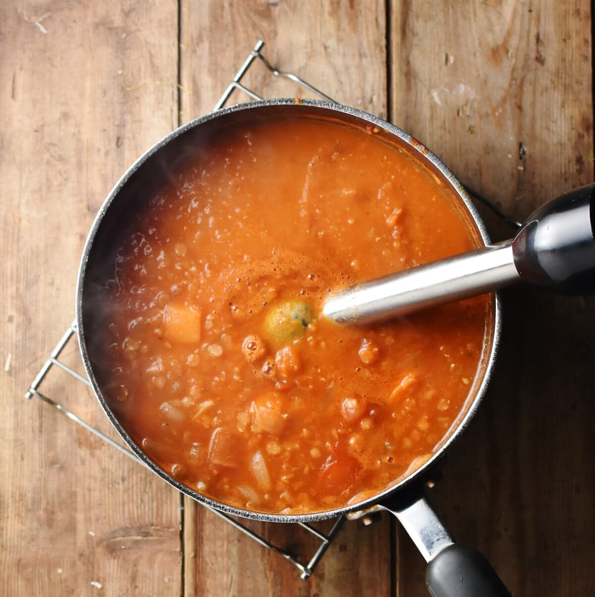 Chunky tomato soup in large pot with stick blender end piece.