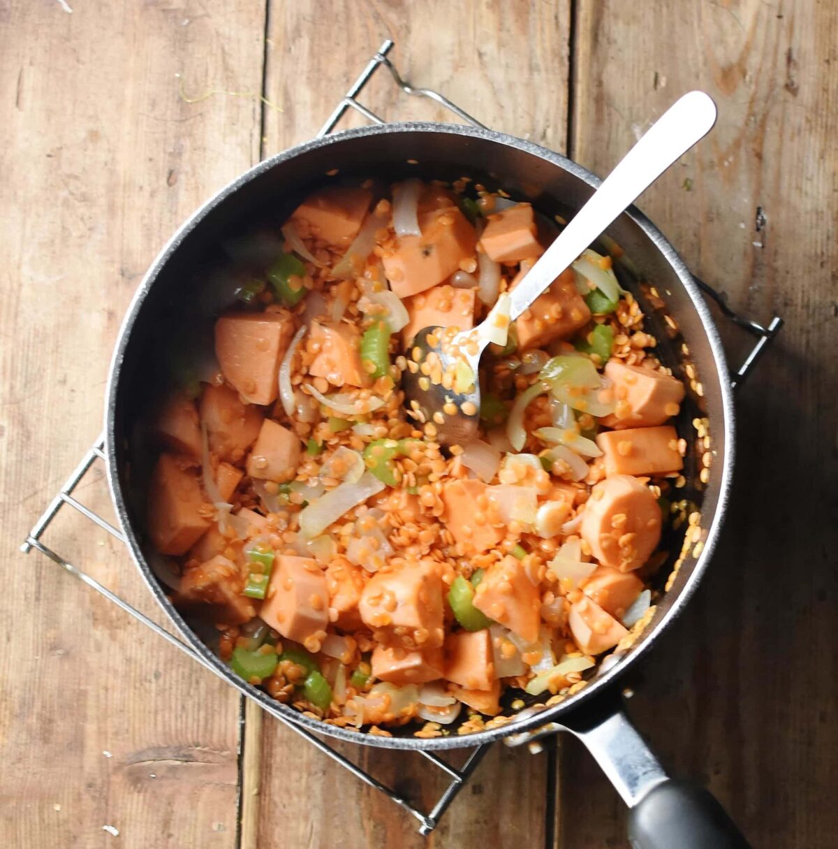 Cubed sweet potato, chopped onions and red lentils in large pot with spoon.