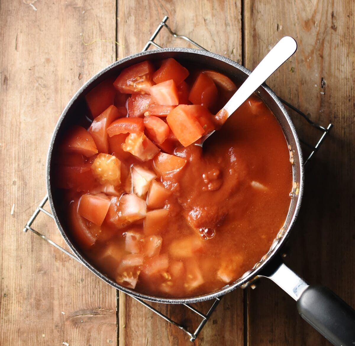 Chopped tomatoes with tomato sauce in large pot with spoon.