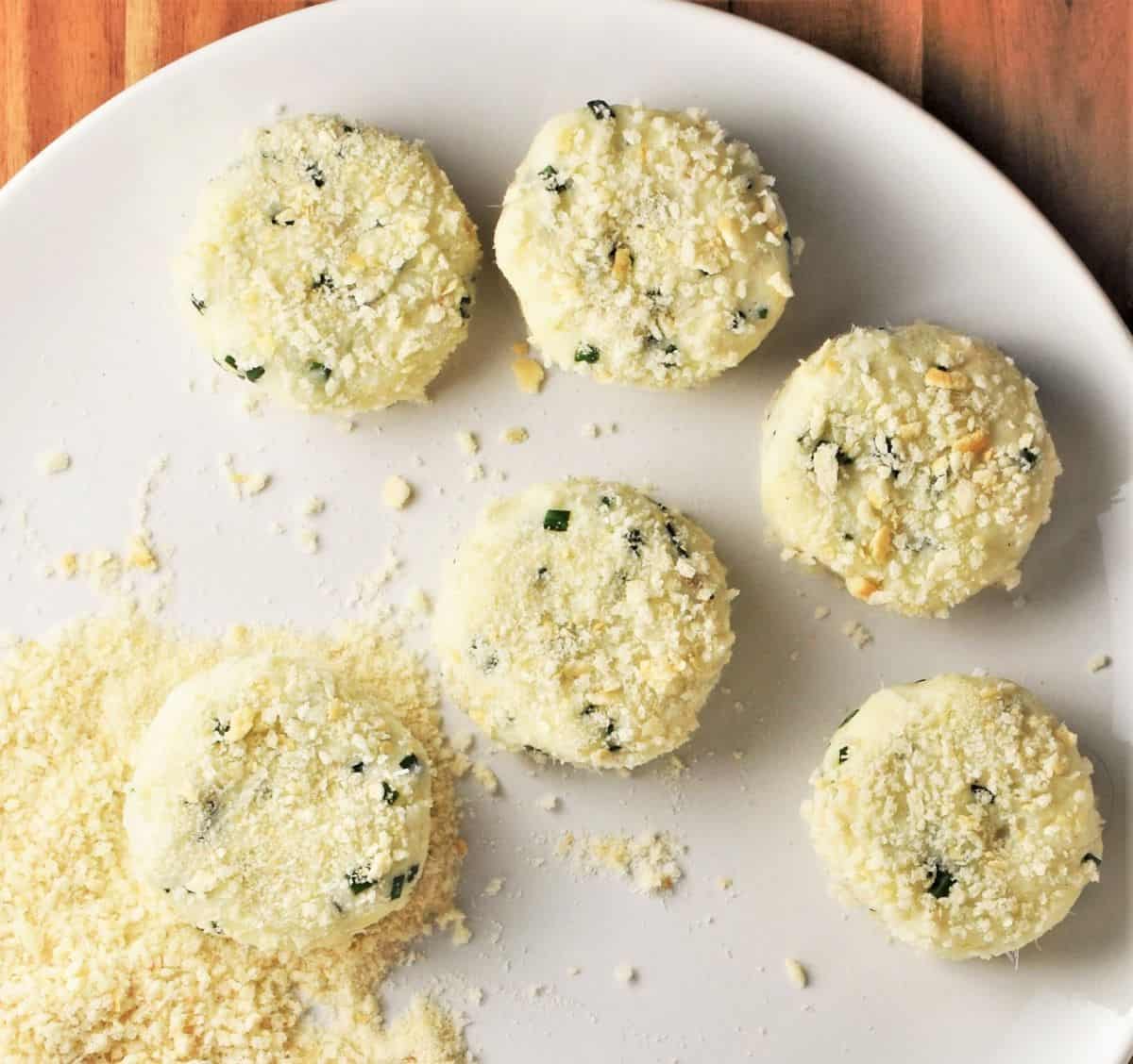 Coating fish cakes with potato in breadcrumbs on top of plate.