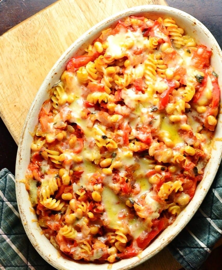 Top down view of bean pasta bake in oval casserole dish on cutting board with green cloth.