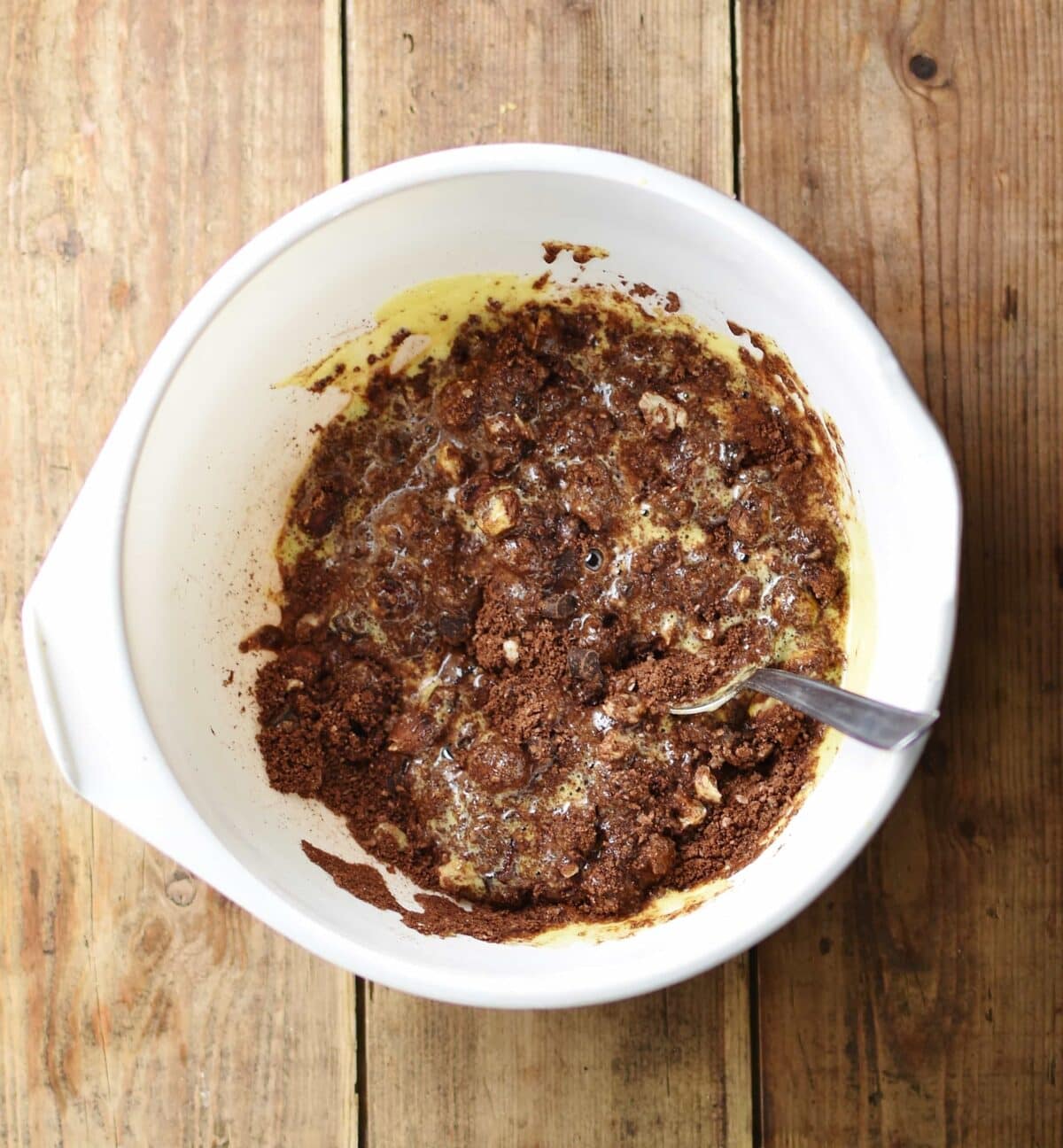 Chocolate cookie mixture with spoon inside large white bowl.