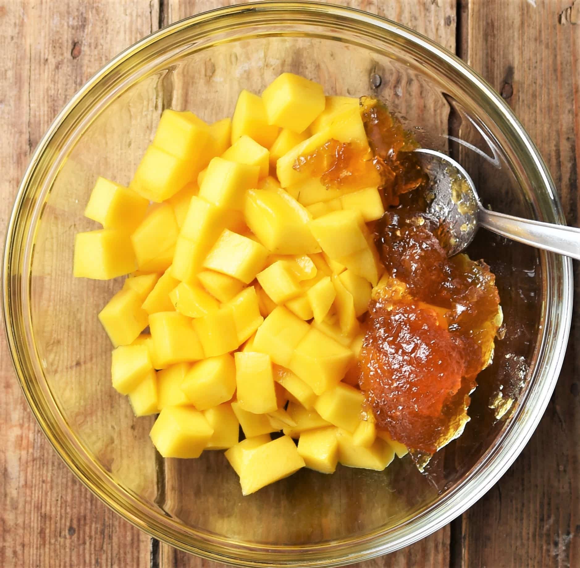 Cubed mango and jam in mixing bowl with spoon.