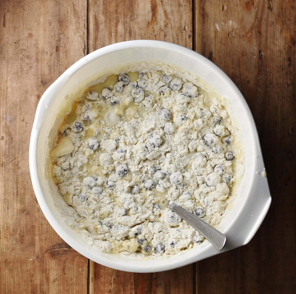Blueberries with flour and egg mixture in large white bowl with spoon.