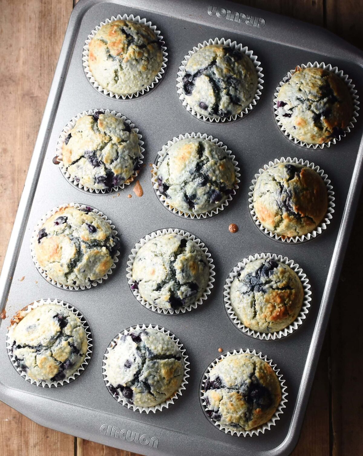 Baked blueberry muffins inside 12-hole muffin pan.