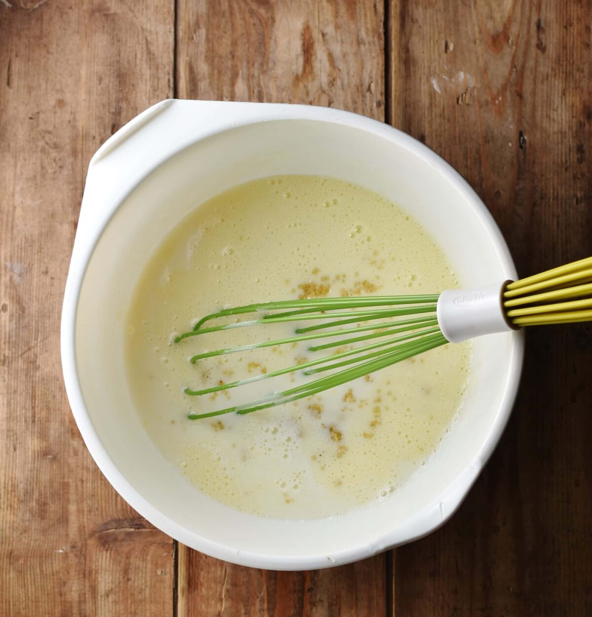 Milk and quinoa mixture in large white bowl with green whisk.