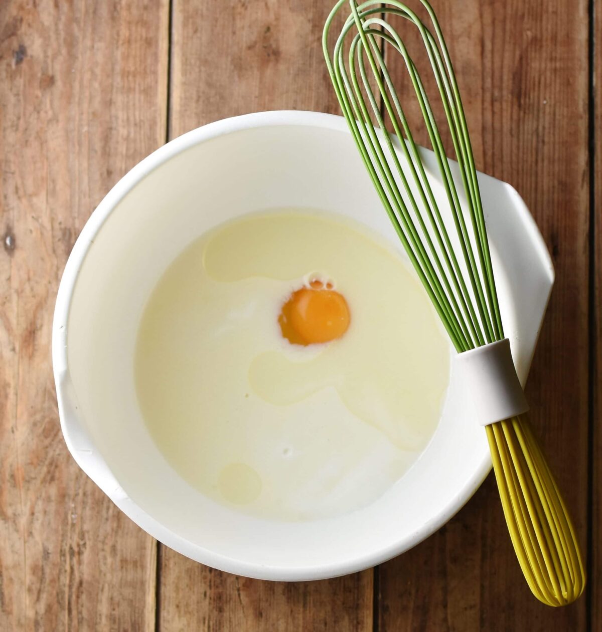Milk and egg mixture in large white bowl with green whisk.