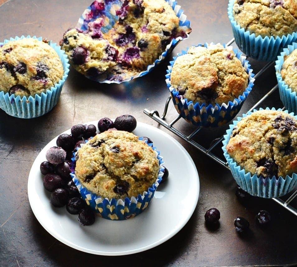Blueberry muffins on top of dark surface with small white plate and cooling rack.