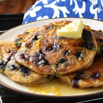 Side view of blueberry ricotta pancakes with butter on top of plate.