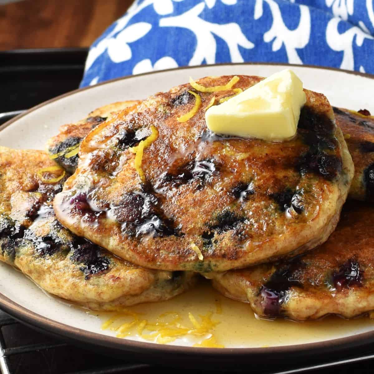 Side view of blueberry ricotta pancakes with butter on top of plate.