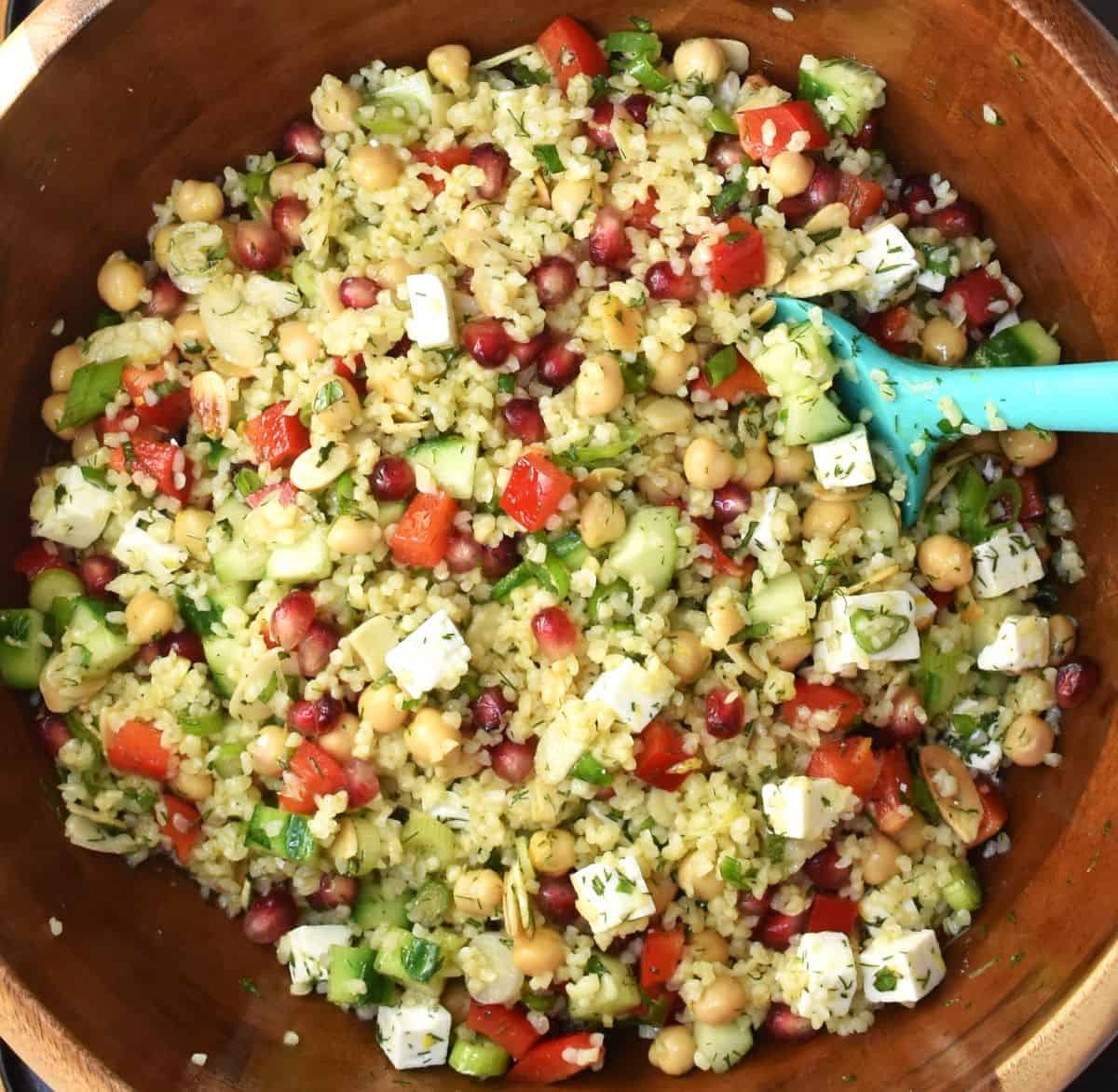 Assembled bulgur salad with lemon dressing in large wooden bowl with blue spatula.