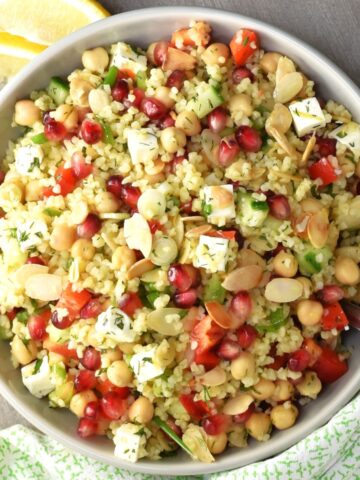 Top down view of bulgur salad with pomegranate seeds, feta and chickpeas in grey bowl.
