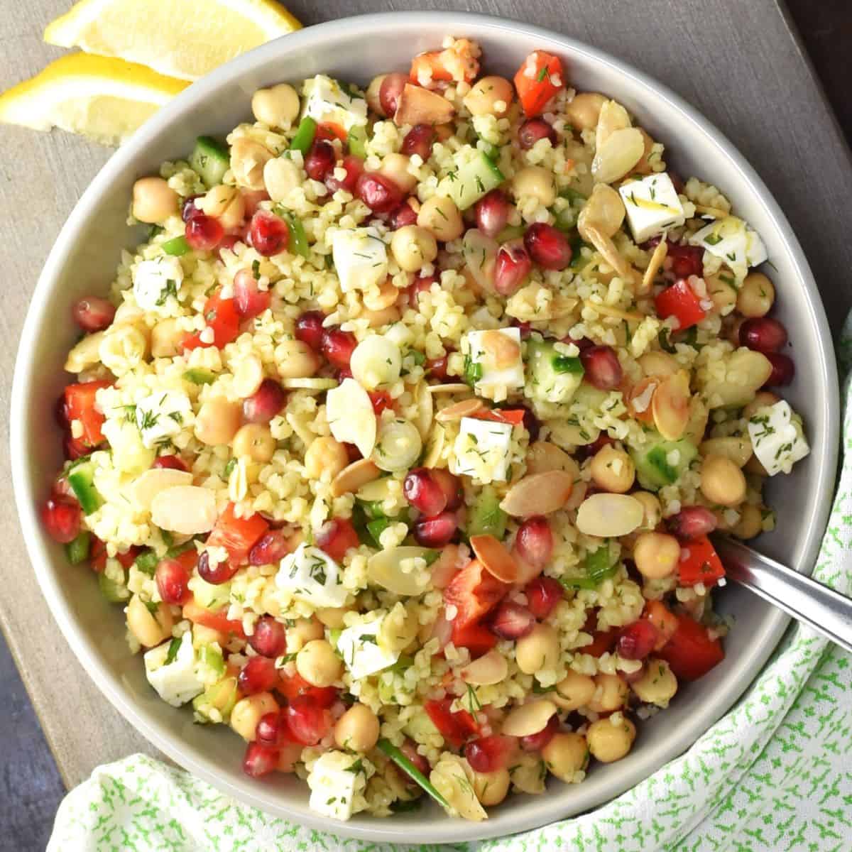 Top down view of bulgur salad with pomegranate seeds, feta and chickpeas in grey bowl.