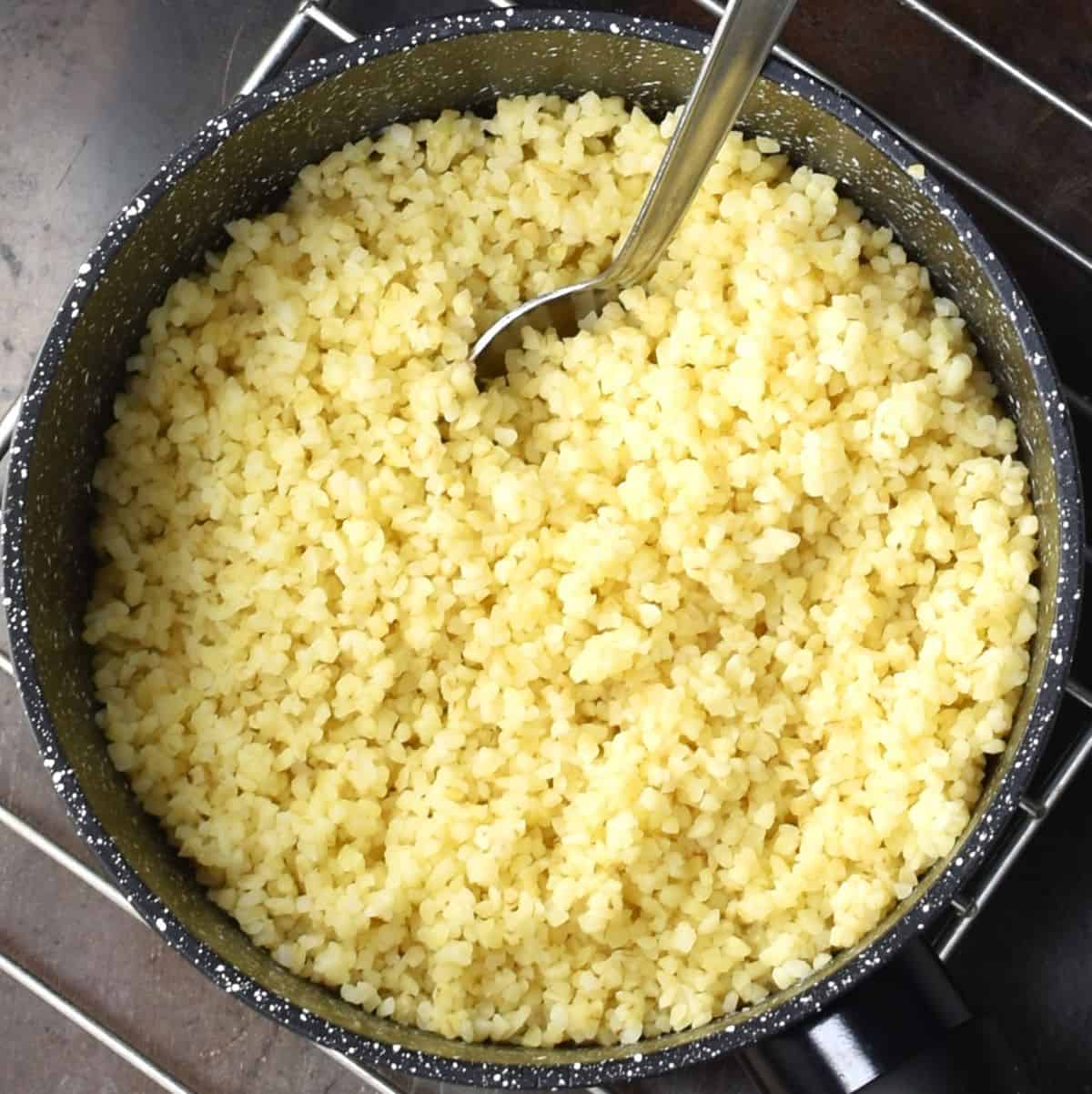 Top down view of cooked bulgur wheat in pan with spoon.
