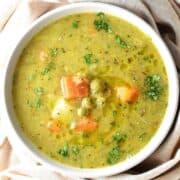 Top down view of canned pea soup with vegetables in white bowl.