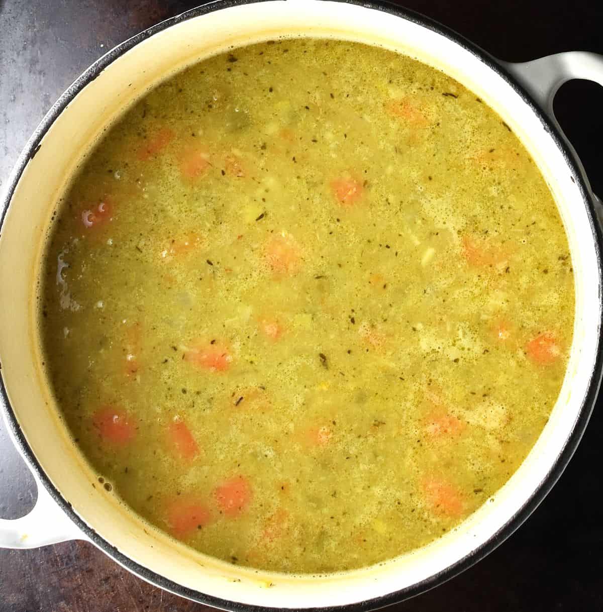 Thick and chunky canned pea soup in white pot.