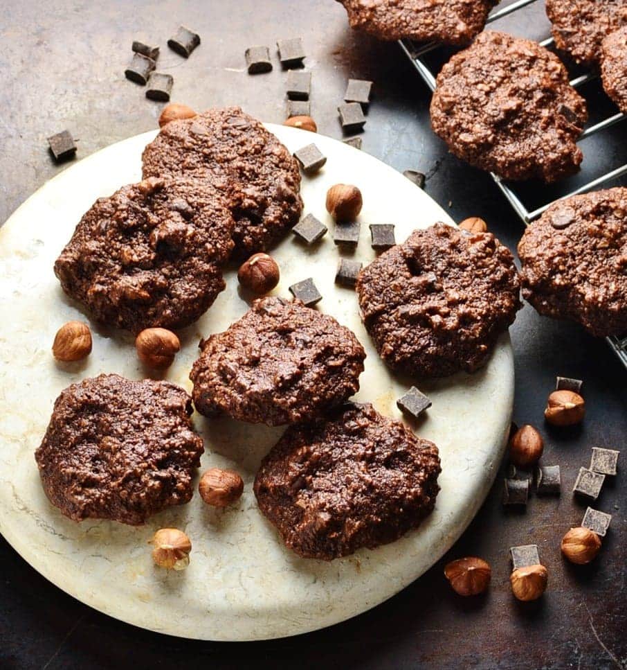 Chocolate hazelnut cookies on white round plate with chocolate chunks and hazelnuts.
