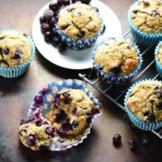 Top down view of quinoa muffins with blueberries on oven tray with small white plate and cooling rack.
