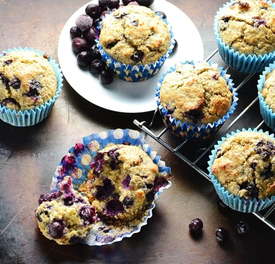 Top down view of blueberry muffins on top of dark surface with small white plate and cooling rack.