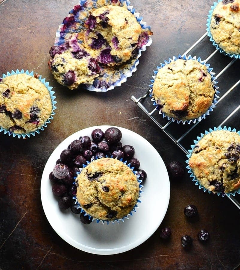 Top down view of blueberry quinoa muffins on top of dark surface with small white plate and cooling rack.
