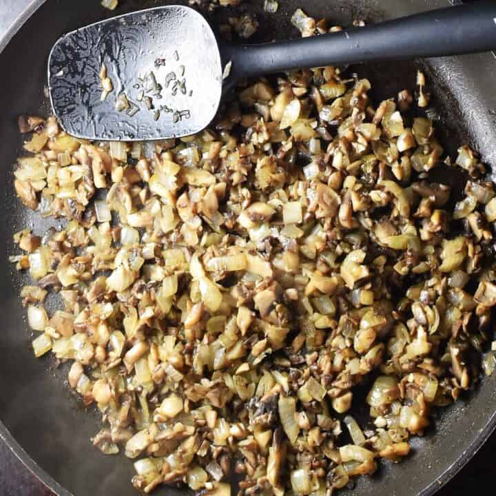 Chopped mushrooms and onion in large pan with black spatula.