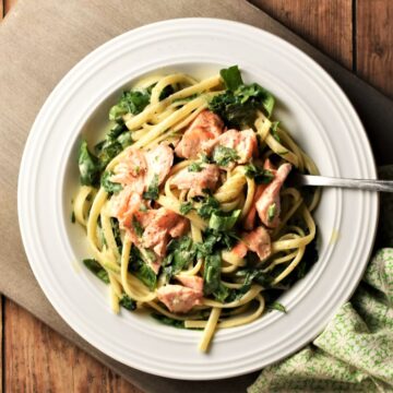 Salmon and spinach with pasta and creamy sauce in white bowl with fork.
