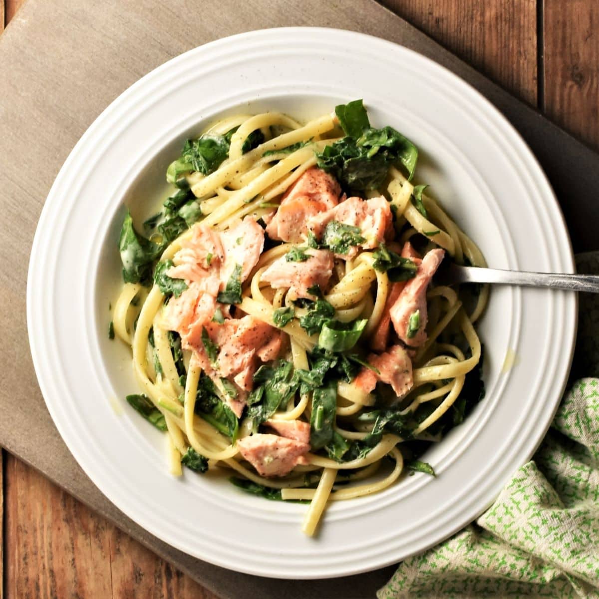 Salmon and spinach with pasta and creamy sauce in white bowl with fork.