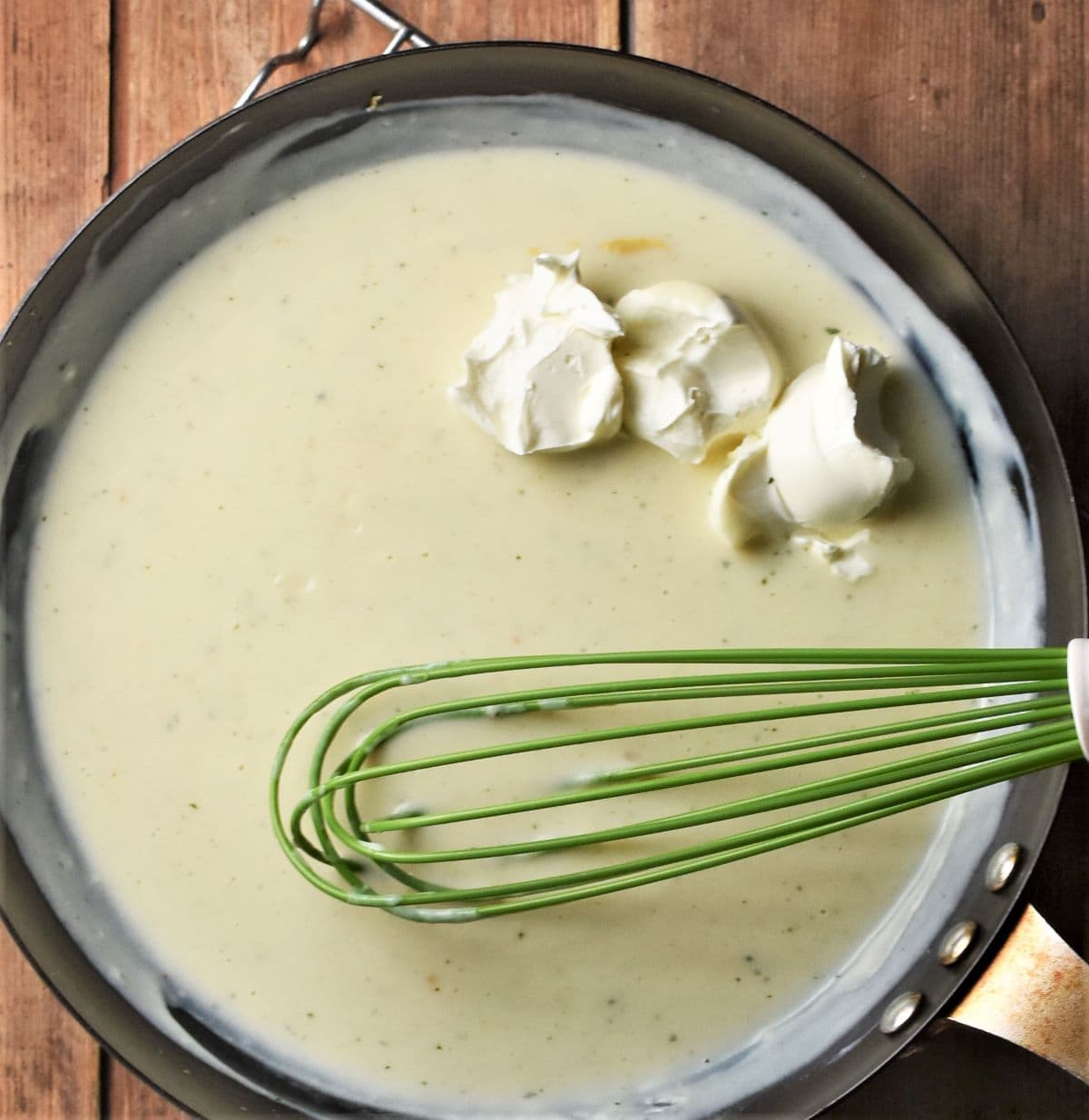 Making creamy sauce with cream cheese in large pan with green whisk.