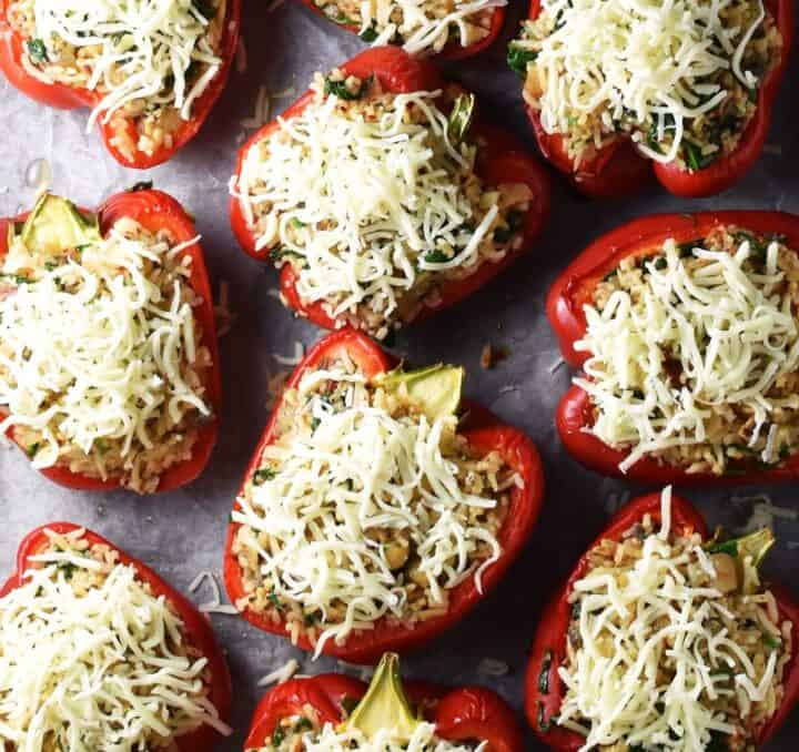 Top down view of red pepper halves with filling and cheese on top.