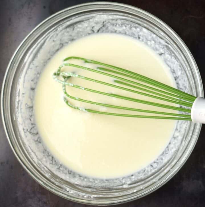Top down view of smooth wet mixture for pancakes in bowl with whisk.