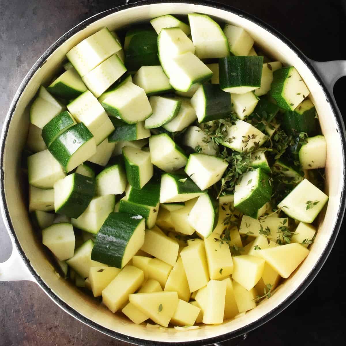 Cubed zucchini and peeled potatoes in large white pot.