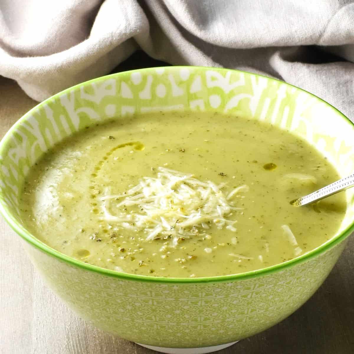 Side view of creamy zucchini potato soup in green bowl with spoon.