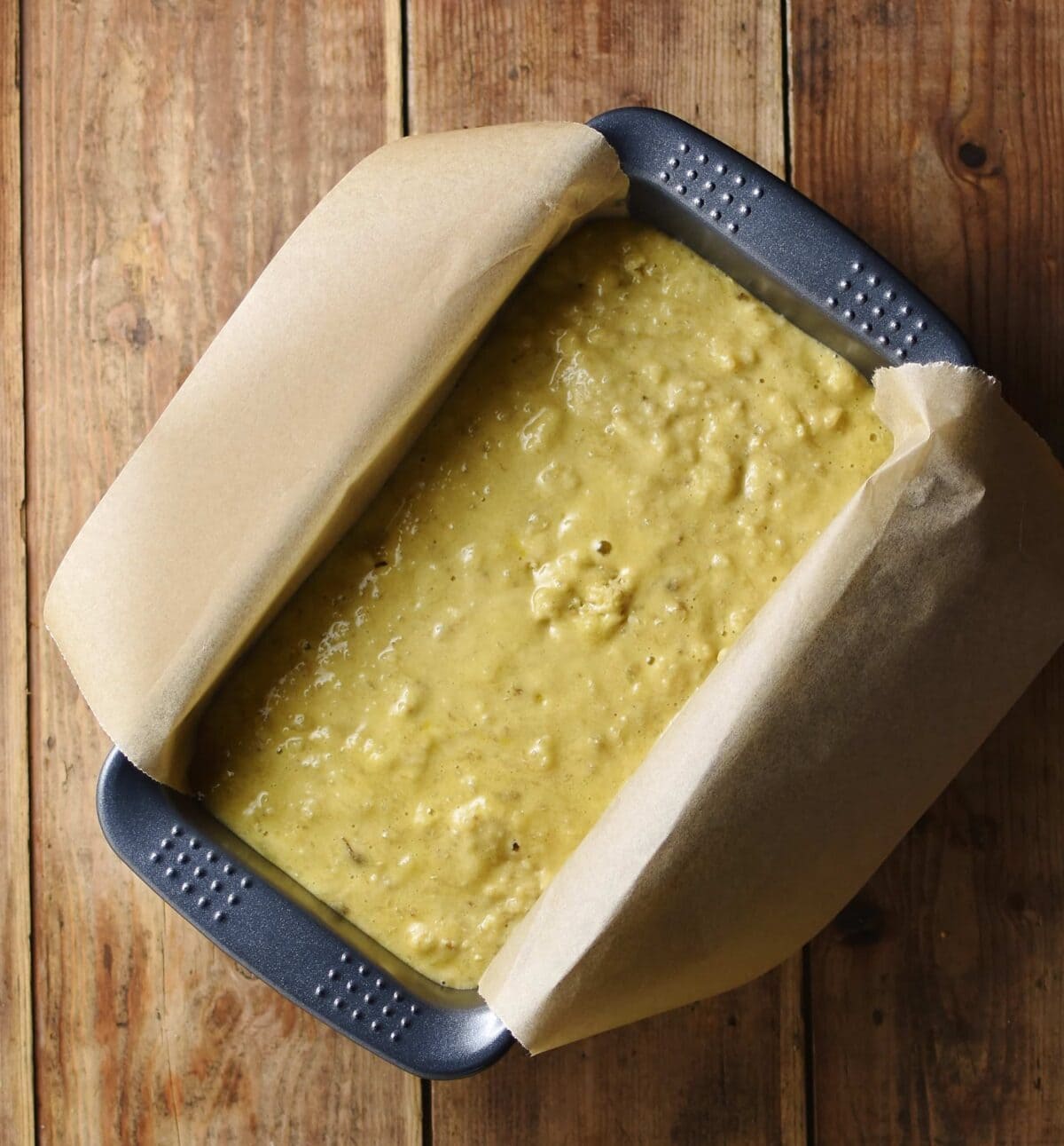Banana bread batter inside bread pan lined with parchment paper.