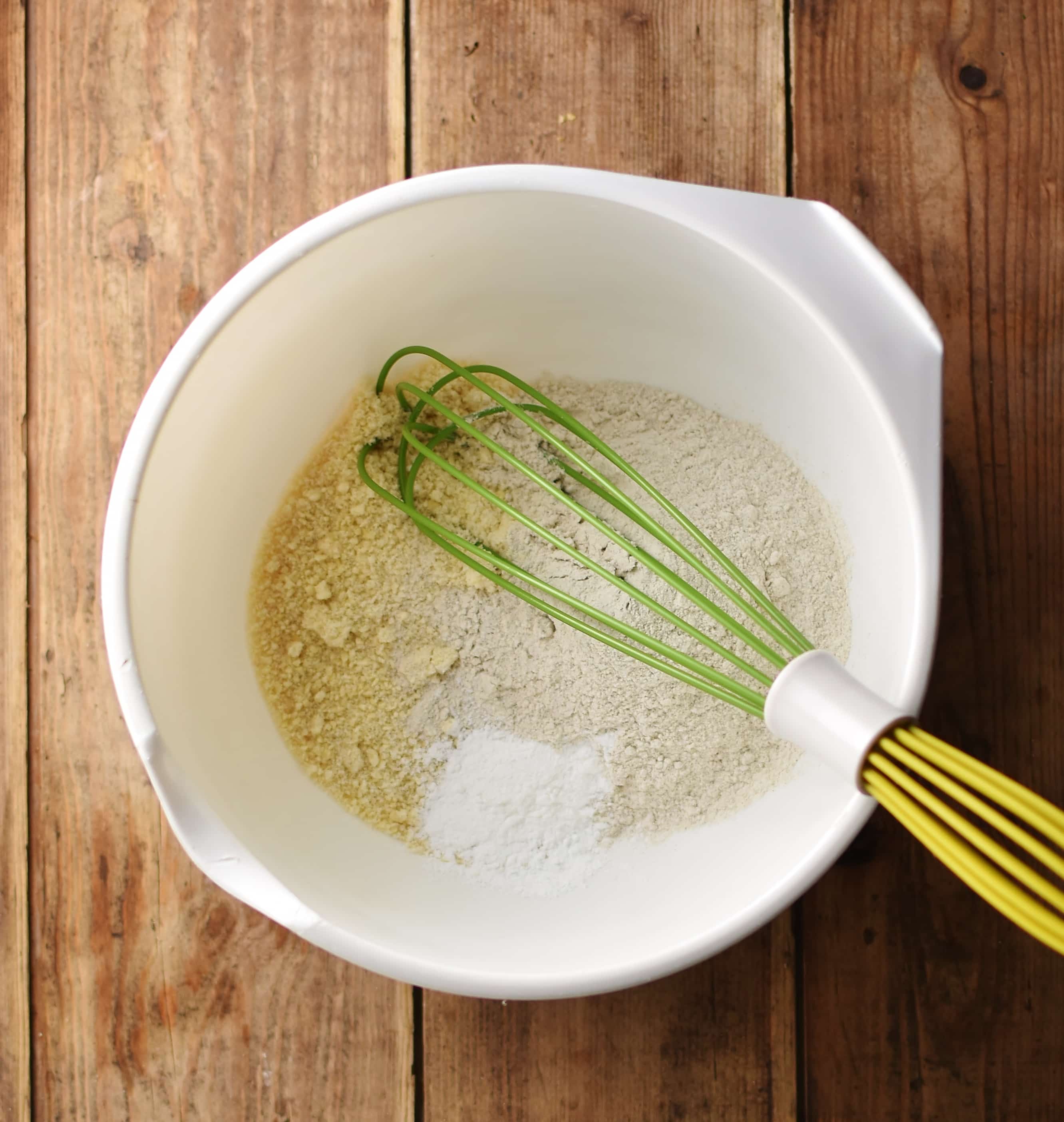 Dry banana bread ingredients with green whisk inside white bowl.
