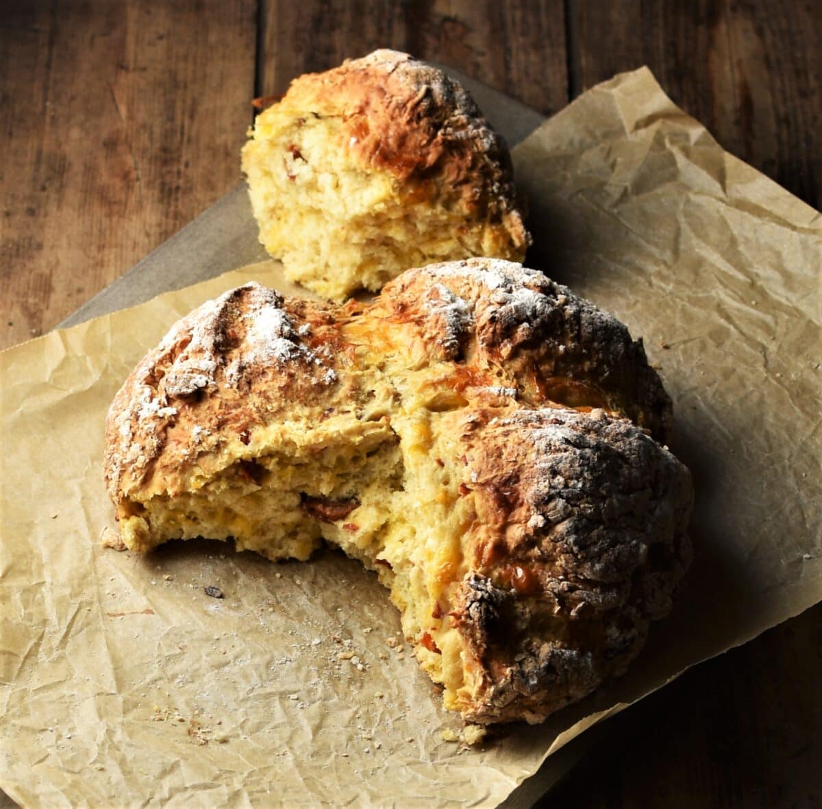 Sun dried tomato soda bread with piece broken off on top of parchment.