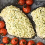 Top down view of cauliflower crusted chicken breast with cherry tomatoes on parchment.