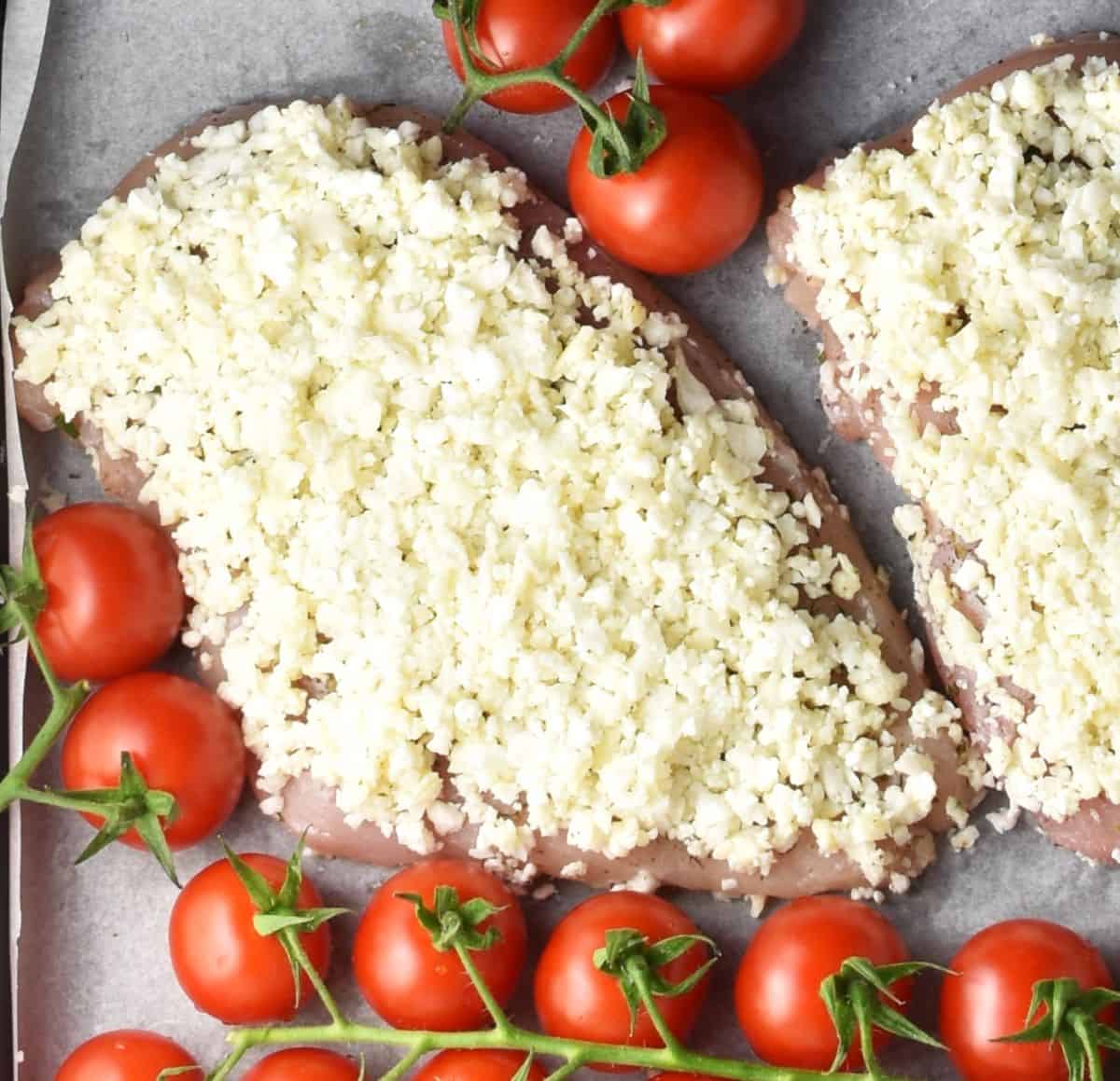 Chicken breast covered with cauliflower crust and surrounded by tomatoes.