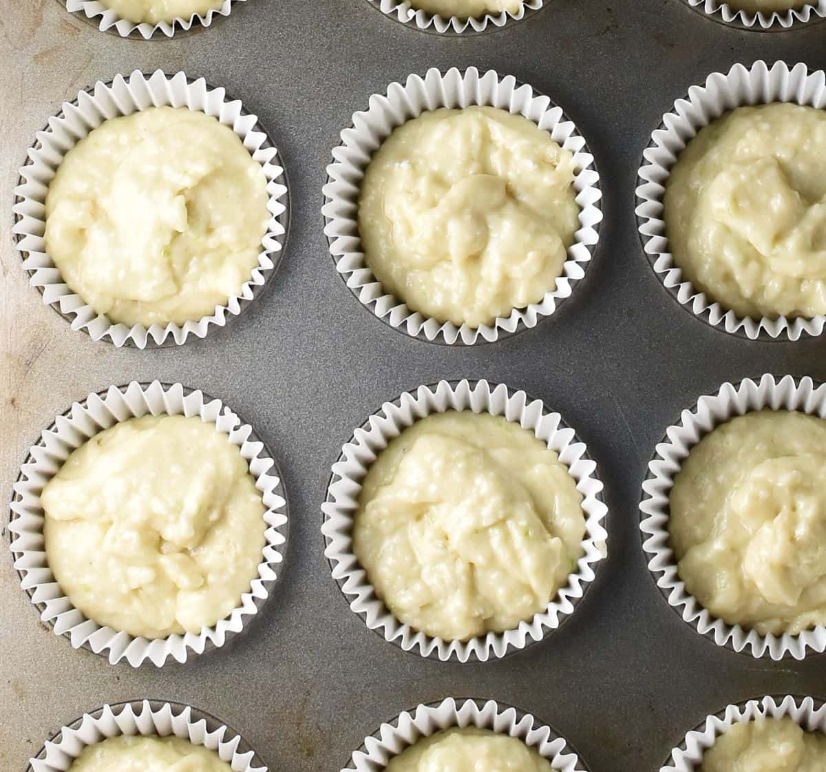 Muffin cases in muffin pan filled with batter.