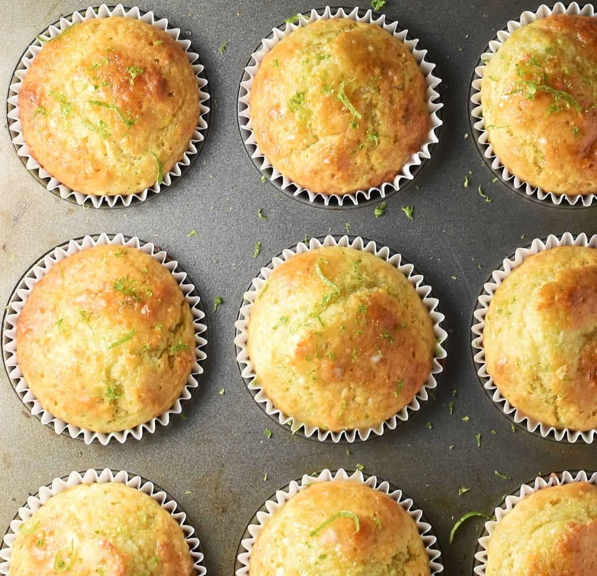 Top down view of baked lime muffins in paper cases in muffin pan.