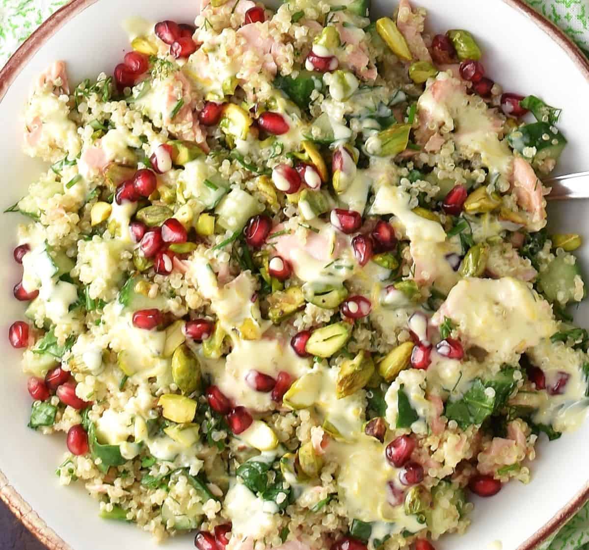 Close-up view of quinoa salmon salad with pomegranate seeds in white bowl.