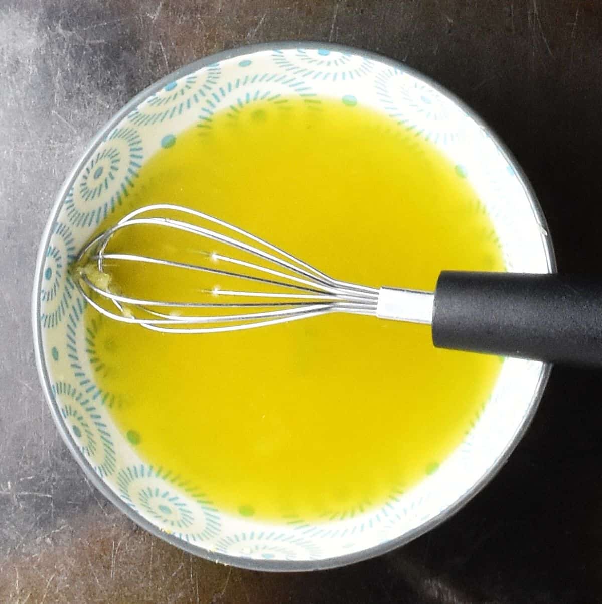 Top down view of salad dressing in blue bowl with whisk.