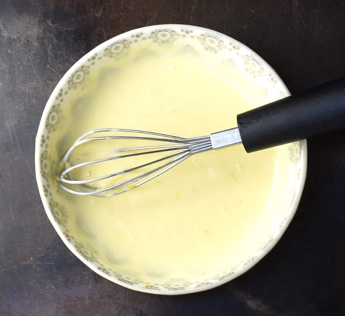 Top down view of creamy dressing in grey bowl with whisk.