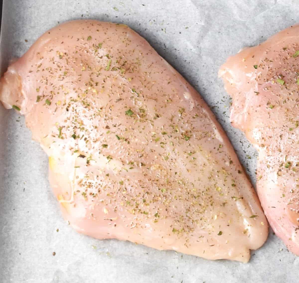Chicken breast with herbs on top of parchment.