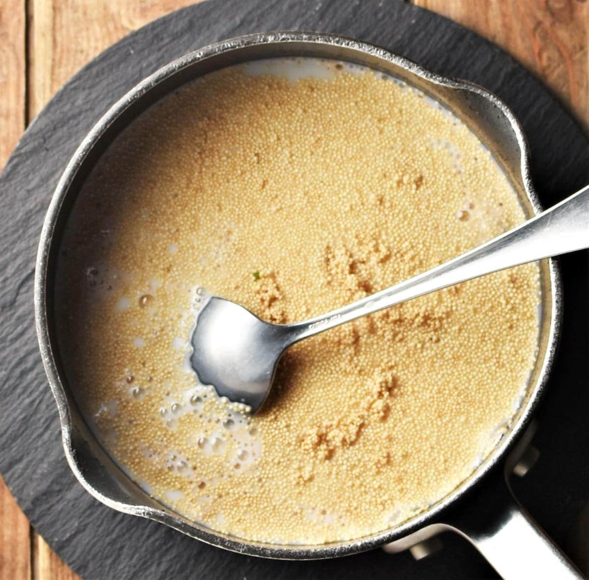Cooking amaranth with milk in saucepan with spoon.